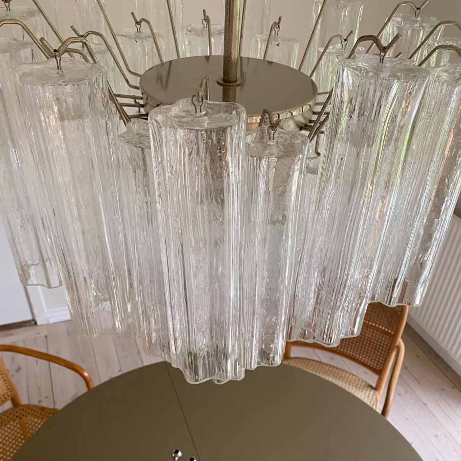Clear glass chandelier hanging above a dining table with chairs.